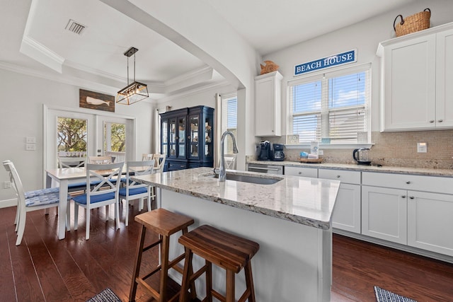 kitchen featuring light stone countertops, sink, white cabinetry, and an island with sink
