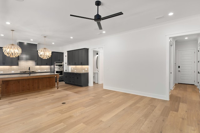 kitchen featuring custom range hood, an island with sink, hanging light fixtures, and light hardwood / wood-style flooring