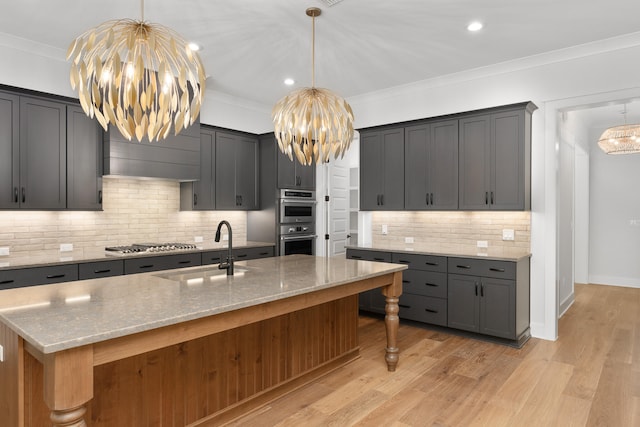 kitchen featuring sink, tasteful backsplash, an island with sink, light hardwood / wood-style floors, and ornamental molding