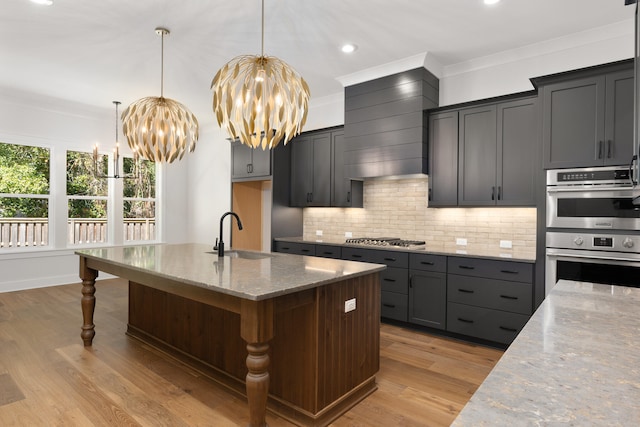 kitchen with light stone countertops, stainless steel appliances, sink, a center island with sink, and an inviting chandelier