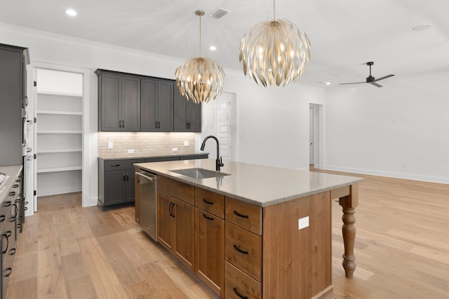 kitchen with sink, light stone counters, light hardwood / wood-style flooring, an island with sink, and ceiling fan with notable chandelier