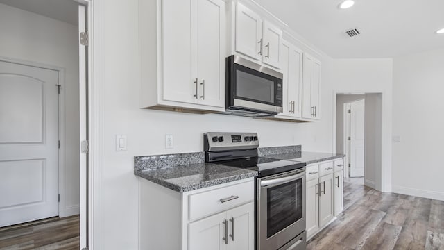 kitchen with white cabinetry, dark stone counters, hardwood / wood-style flooring, and appliances with stainless steel finishes