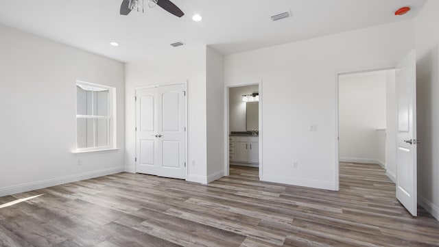 unfurnished bedroom with ceiling fan, a closet, wood-type flooring, and ensuite bath