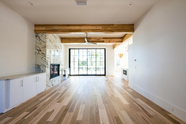 unfurnished living room with beamed ceiling, ceiling fan, and light hardwood / wood-style flooring