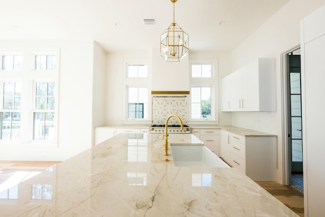 kitchen featuring light stone countertops, pendant lighting, white cabinets, and sink