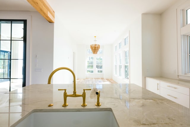 room details featuring white cabinets, pendant lighting, light stone counters, and sink