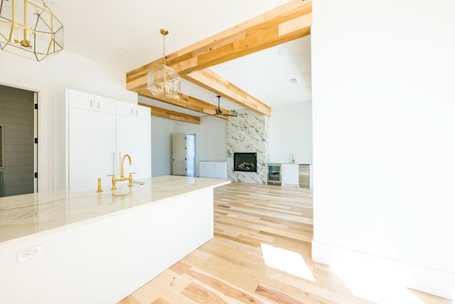 kitchen featuring beam ceiling, a fireplace, white cabinets, and hanging light fixtures