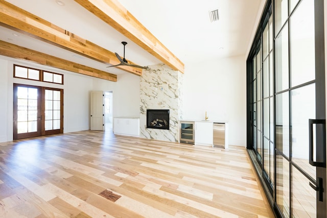 unfurnished living room featuring french doors, ceiling fan, beam ceiling, a fireplace, and light hardwood / wood-style floors