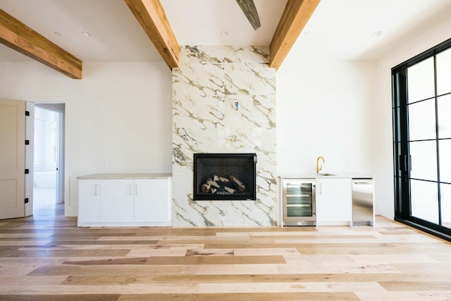 unfurnished living room featuring beam ceiling, sink, beverage cooler, a premium fireplace, and light wood-type flooring