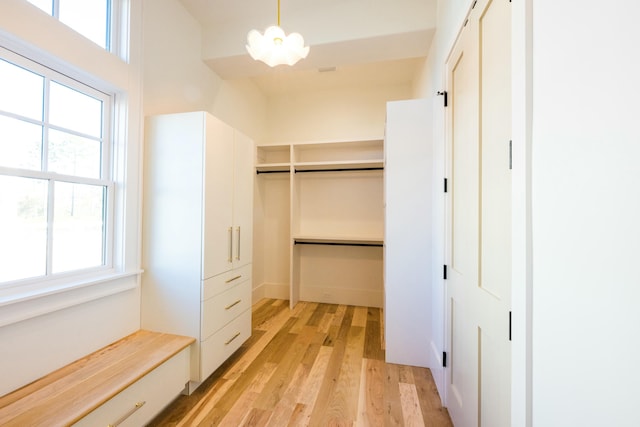 spacious closet with light hardwood / wood-style floors and an inviting chandelier