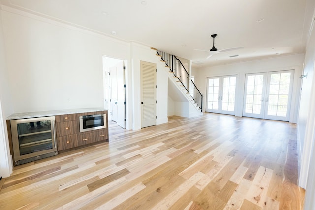 unfurnished living room featuring ceiling fan, french doors, beverage cooler, light wood-type flooring, and ornamental molding