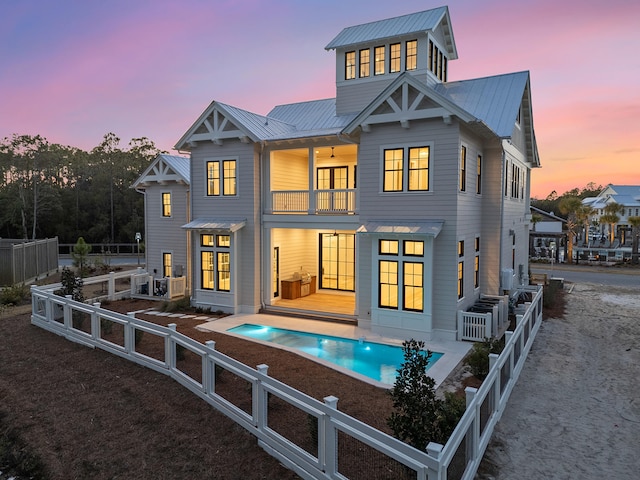 back house at dusk featuring a balcony, a fenced in pool, and a patio area