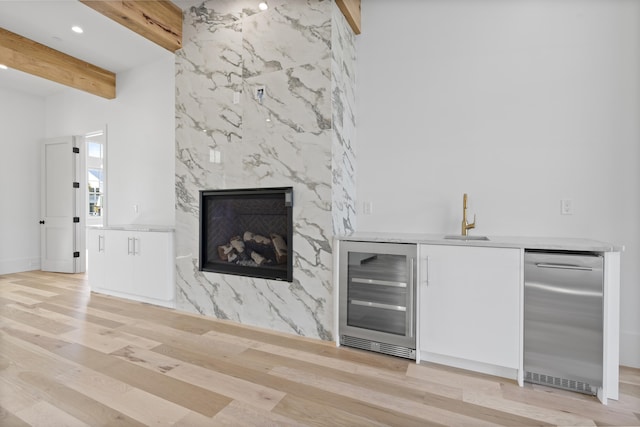 bar featuring sink, beverage cooler, a high end fireplace, light hardwood / wood-style floors, and beam ceiling