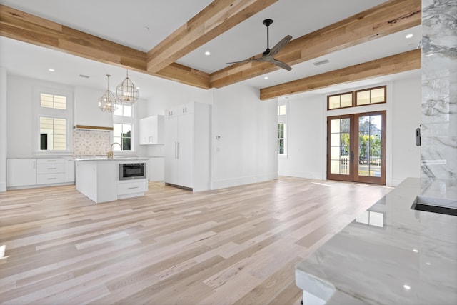 living room featuring beamed ceiling, a wealth of natural light, light hardwood / wood-style floors, and french doors