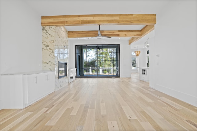 unfurnished living room featuring plenty of natural light, a high end fireplace, beamed ceiling, and light wood-type flooring