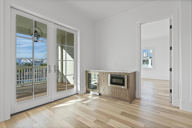 interior space featuring ornamental molding, light hardwood / wood-style floors, beverage cooler, and french doors