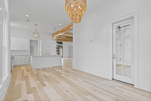 unfurnished living room featuring an inviting chandelier, sink, beam ceiling, and light hardwood / wood-style floors