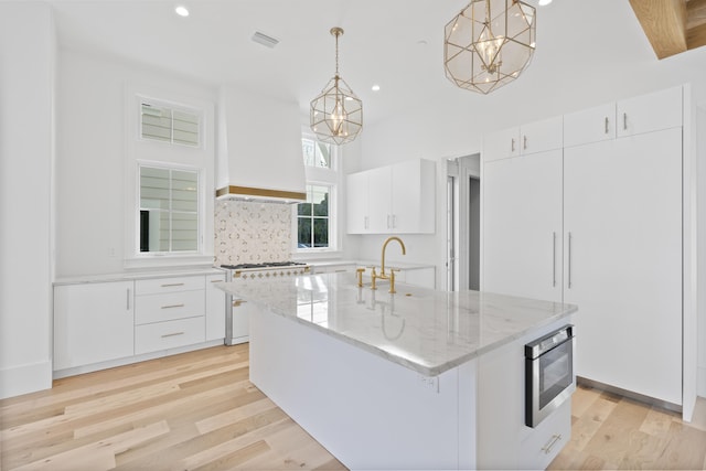 kitchen featuring premium range hood, pendant lighting, range with gas stovetop, white cabinetry, and a center island with sink