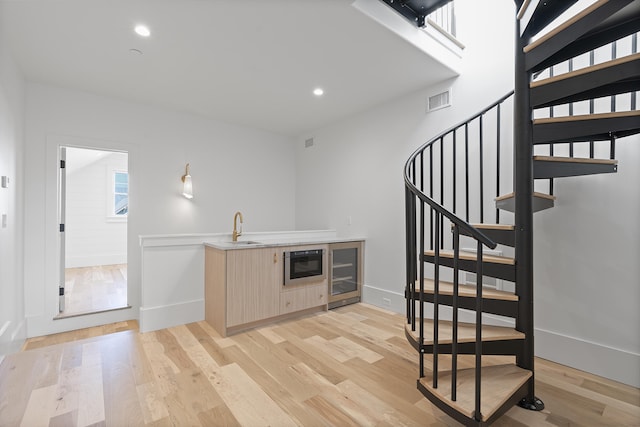 bar with beverage cooler, light brown cabinetry, sink, and light wood-type flooring