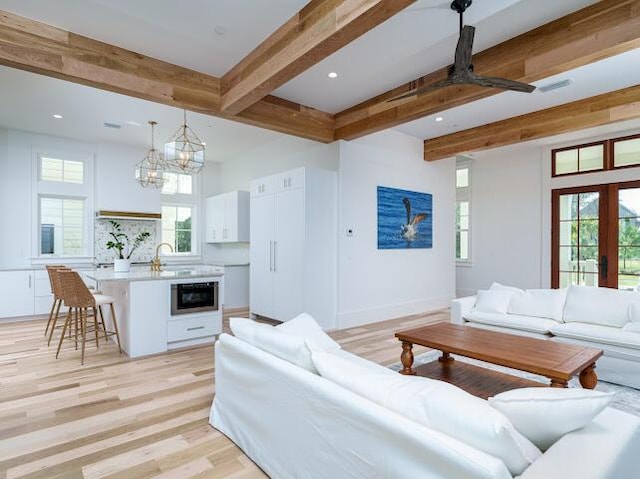 living room with a healthy amount of sunlight, light wood-style floors, beamed ceiling, and ceiling fan with notable chandelier