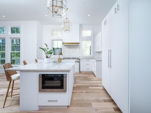 kitchen featuring white cabinets, a center island with sink, a chandelier, a kitchen bar, and stainless steel oven