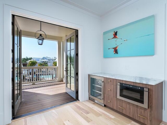 doorway to outside featuring ornamental molding, beverage cooler, and light wood-type flooring
