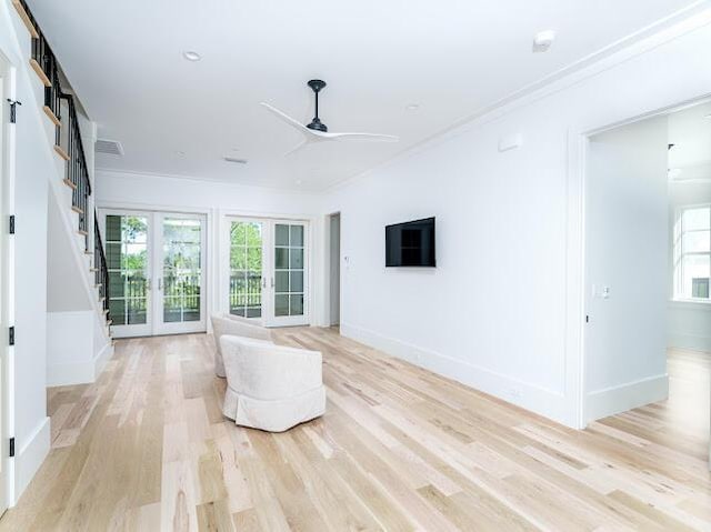 unfurnished living room with light wood-style flooring, baseboards, a ceiling fan, stairway, and crown molding
