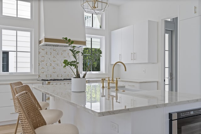 114 Climbing Rose Way, Santa Rosa Beach, FL 32459 - kitchen featuring premium range hood, white cabinets, a kitchen bar, light stone countertops, and decorative backsplash