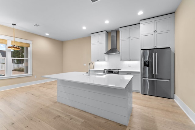 kitchen with wall chimney exhaust hood, sink, stainless steel appliances, and a kitchen island with sink