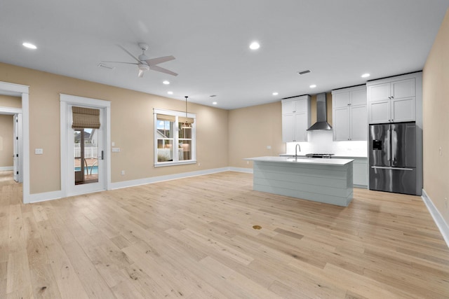 kitchen featuring sink, wall chimney range hood, stainless steel refrigerator with ice dispenser, light hardwood / wood-style floors, and a center island with sink