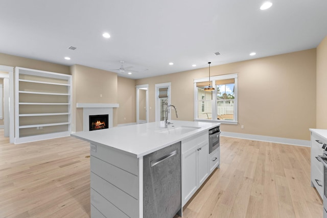 kitchen featuring appliances with stainless steel finishes, a kitchen island with sink, sink, decorative light fixtures, and light hardwood / wood-style floors