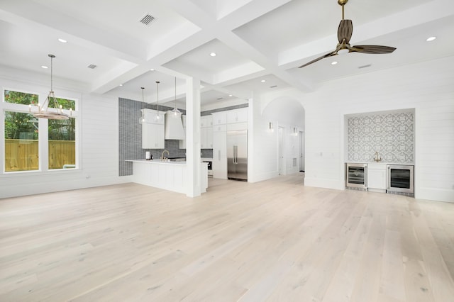 unfurnished living room with ceiling fan, beam ceiling, light wood-type flooring, and wine cooler