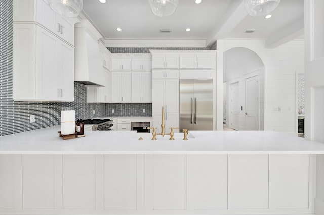 kitchen with custom exhaust hood, white cabinets, appliances with stainless steel finishes, beam ceiling, and kitchen peninsula