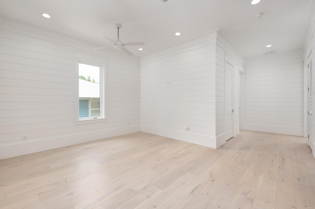 unfurnished room with light wood-type flooring, ceiling fan, and wood walls