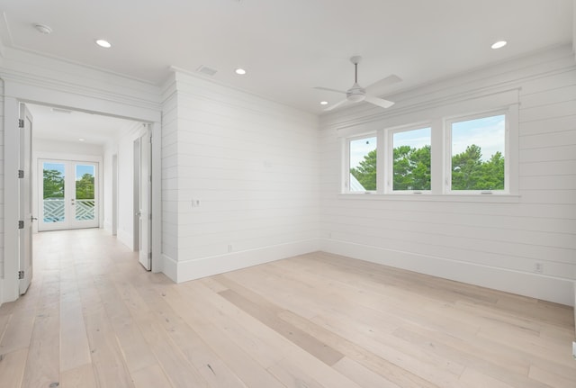 spare room featuring french doors, light hardwood / wood-style flooring, a wealth of natural light, and wood walls