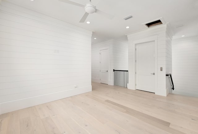 empty room with light hardwood / wood-style floors, ceiling fan, and wooden walls