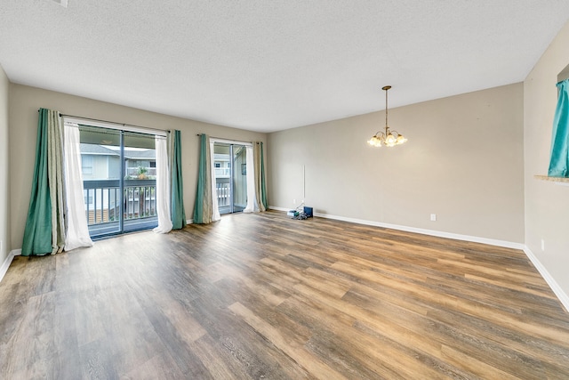 empty room with wood-type flooring, a textured ceiling, and a notable chandelier