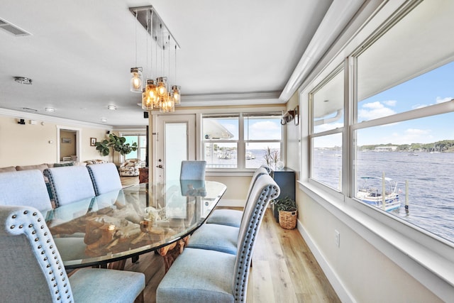 dining room with a chandelier, a water view, ornamental molding, and light hardwood / wood-style flooring