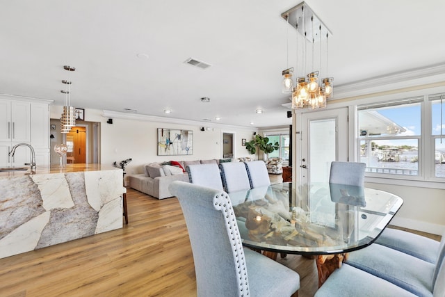 dining space with a notable chandelier, ornamental molding, sink, and light hardwood / wood-style flooring