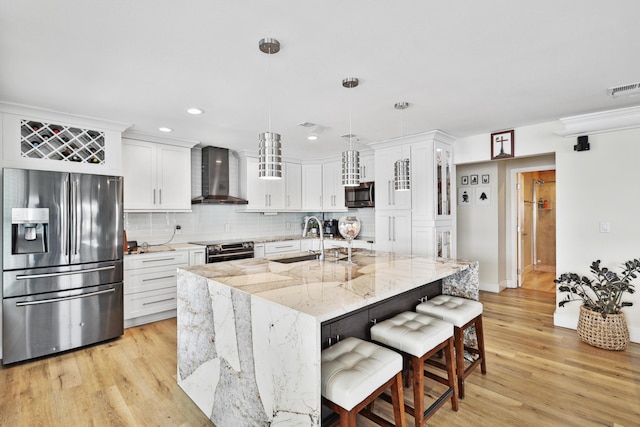 kitchen with a kitchen island with sink, wall chimney range hood, sink, decorative light fixtures, and stainless steel appliances