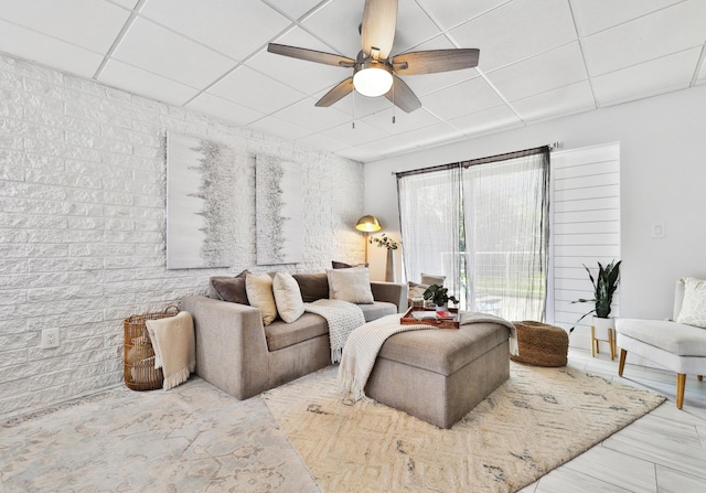 living room with ceiling fan, a drop ceiling, and brick wall