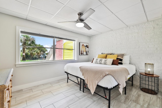 bedroom featuring a paneled ceiling, ceiling fan, and brick wall