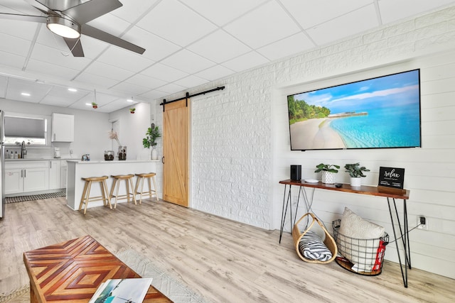 living room with a paneled ceiling, sink, ceiling fan, a barn door, and light hardwood / wood-style floors