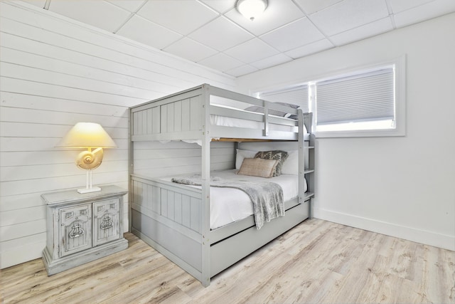 bedroom with a paneled ceiling, wood walls, and light wood-type flooring