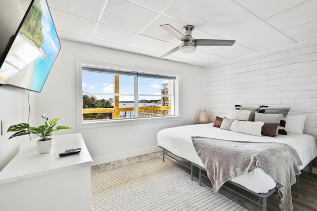 bedroom featuring hardwood / wood-style floors, ceiling fan, wooden walls, and a drop ceiling