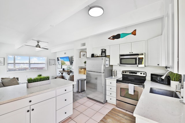 kitchen with appliances with stainless steel finishes, ceiling fan, light tile patterned floors, beam ceiling, and white cabinets