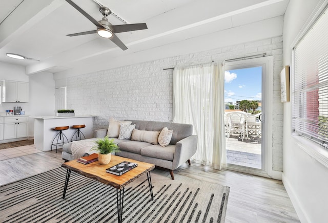 living room with ceiling fan, beamed ceiling, brick wall, and light wood-type flooring