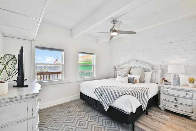 bedroom with beamed ceiling, ceiling fan, brick wall, and light hardwood / wood-style flooring