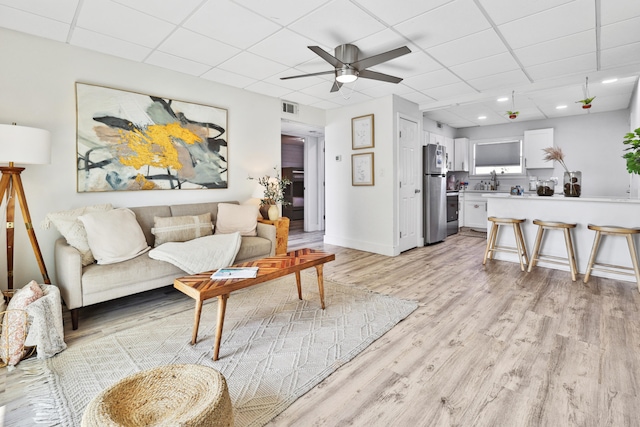 living room with a paneled ceiling, ceiling fan, and light hardwood / wood-style flooring