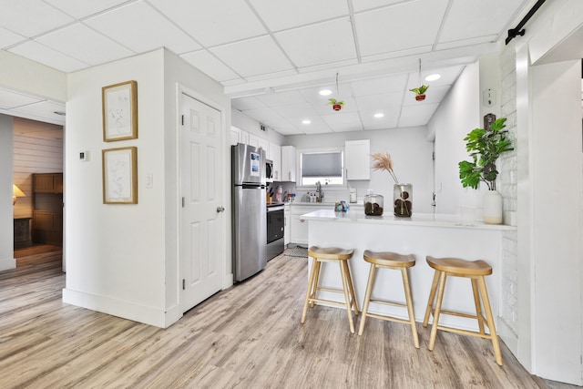 kitchen featuring kitchen peninsula, appliances with stainless steel finishes, a kitchen breakfast bar, a barn door, and white cabinets